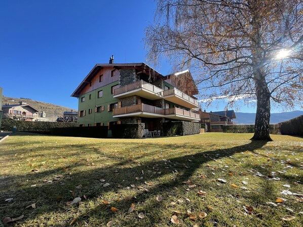 A multi-story building with balconies and a stone facade, surrounded by a well-maintained lawn and trees.