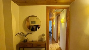 Un pasillo con suelo de madera, un espejo en la pared, una mesita con un jarrón y una vela, y una cesta en el suelo.