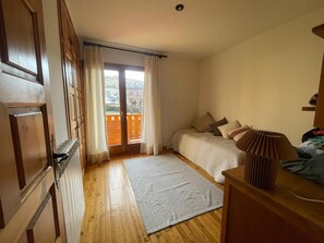 A bedroom with a wooden floor, a bed with pillows, a window with curtains, and a balcony.