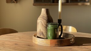 Una mesa de madera con una vela, un tarro de vidrio verde y un jarrón de madera.