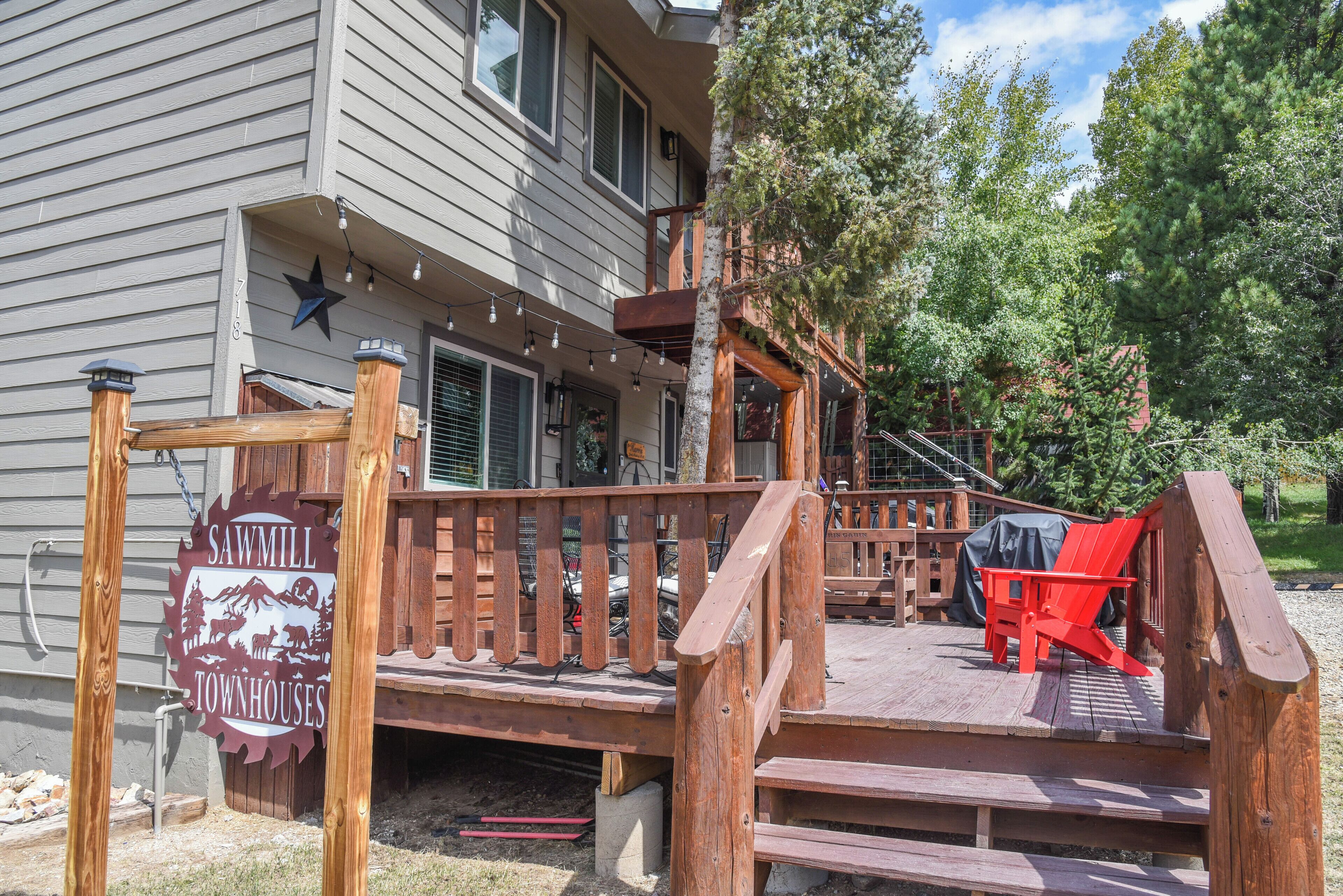 A wooden deck with a sign reading "Sawmill Townhouses," a red chair, and a covered area with a table.