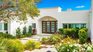 A modern white building with a large arched entrance, surrounded by a well-maintained garden with various plants and flowers. - La Jolla Dream Stay: Ocean, Bay, Pool (San Diego)