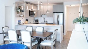 Une cuisine moderne dotée d’un îlot central, de meubles blancs, d’appareils électroménagers en acier inoxydable et de luminaires suspendus.
