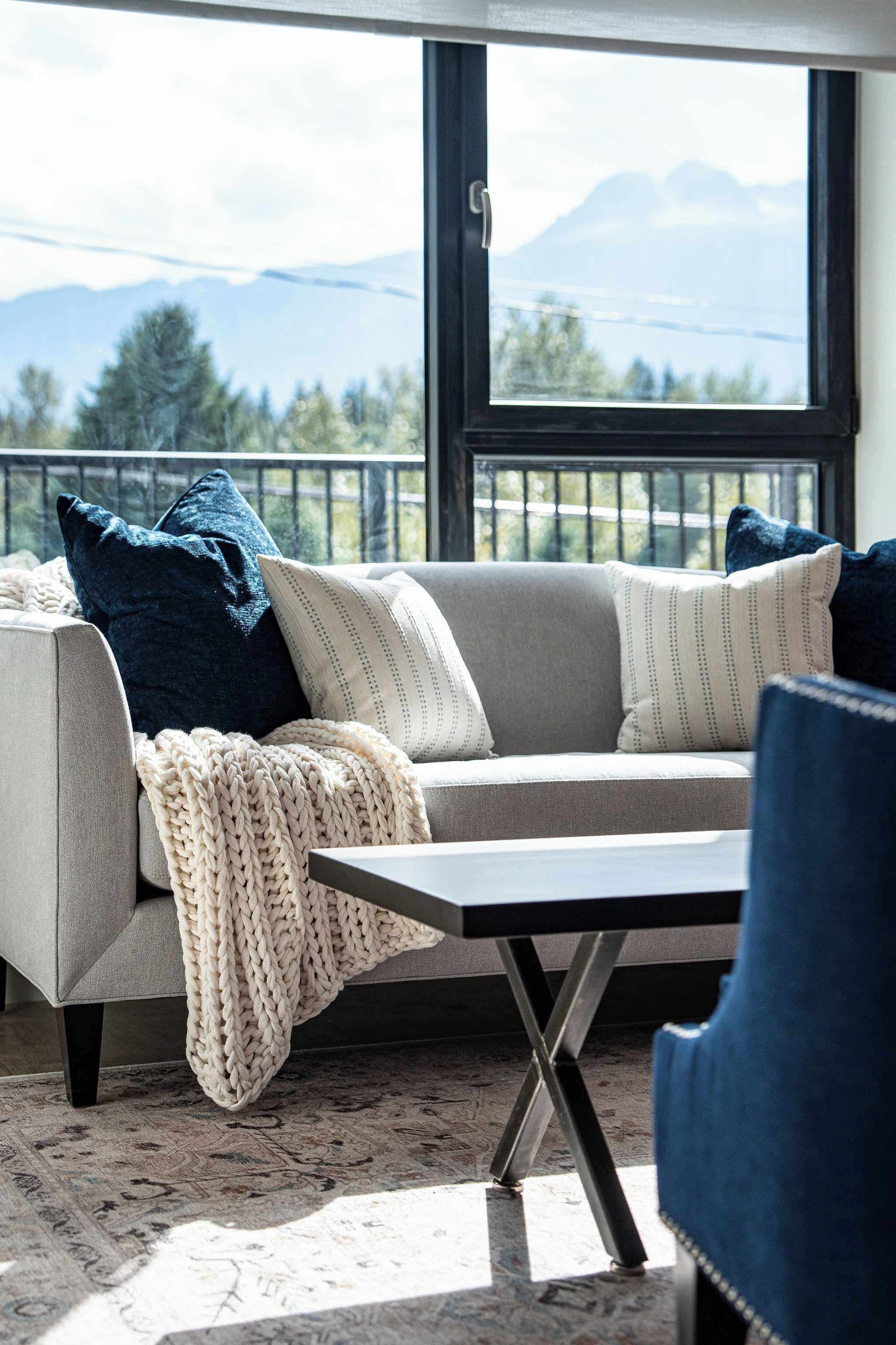 A modern living room with a sofa, a coffee table, and a view of mountains through a large window.
