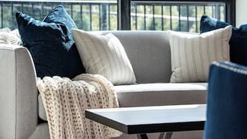 A modern living room with a sofa, a coffee table, and a view of mountains through a large window.