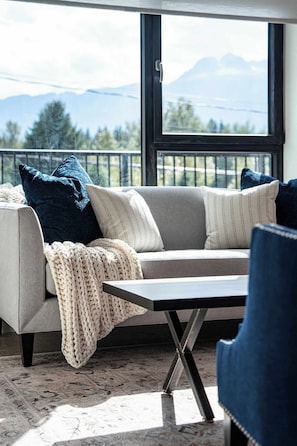 A modern living room with a sofa, a coffee table, and a view of mountains through a large window.