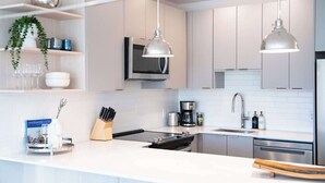 Une cuisine moderne avec des meubles blancs, des appareils en acier inoxydable et des luminaires suspendus.