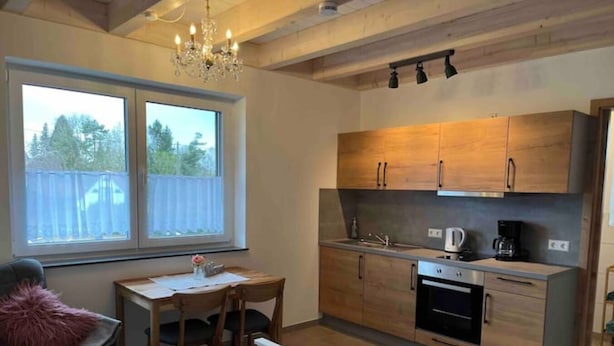 Een kleine keuken met houten kastjes, een eettafel en een kroonluchter.