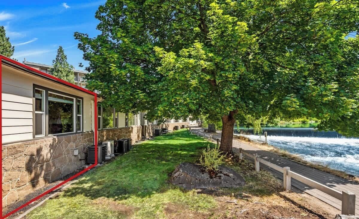 A riverside property with a stone wall, a wooden deck, and a grassy area.