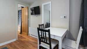 A small, clean room with a white desk, a chair, a TV mounted on the wall, and a door leading to another room.