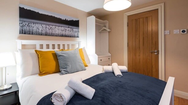 A neatly arranged bedroom with a bed, bedside tables, a hanging light, and a door.