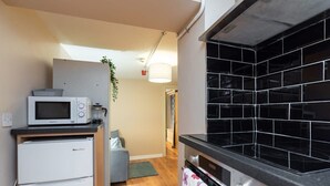 A compact kitchen with a microwave, refrigerator, and black tiled backsplash.