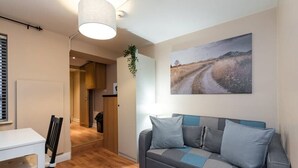 A modern living room with a grey sofa, a white table, and a painting of a rural road.