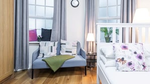 A modern room with a grey sofa, a white bed, a clock on the wall, and a window with curtains. - Cosy citycentre flat with TV & Wi-Fi included (Dublin 1)