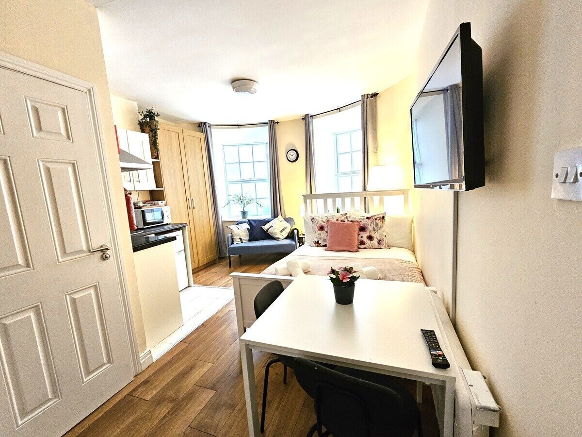 A compact living space with a kitchenette, a dining area, a sofa, and a TV mounted on the wall.