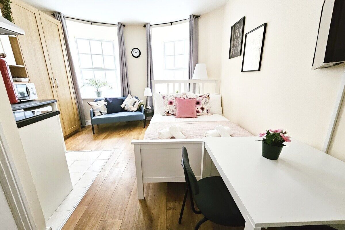A compact bedroom with a bed, bedside table, chair, and a desk.