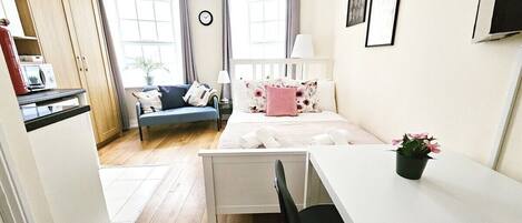 A compact bedroom with a bed, bedside table, chair, and a desk.