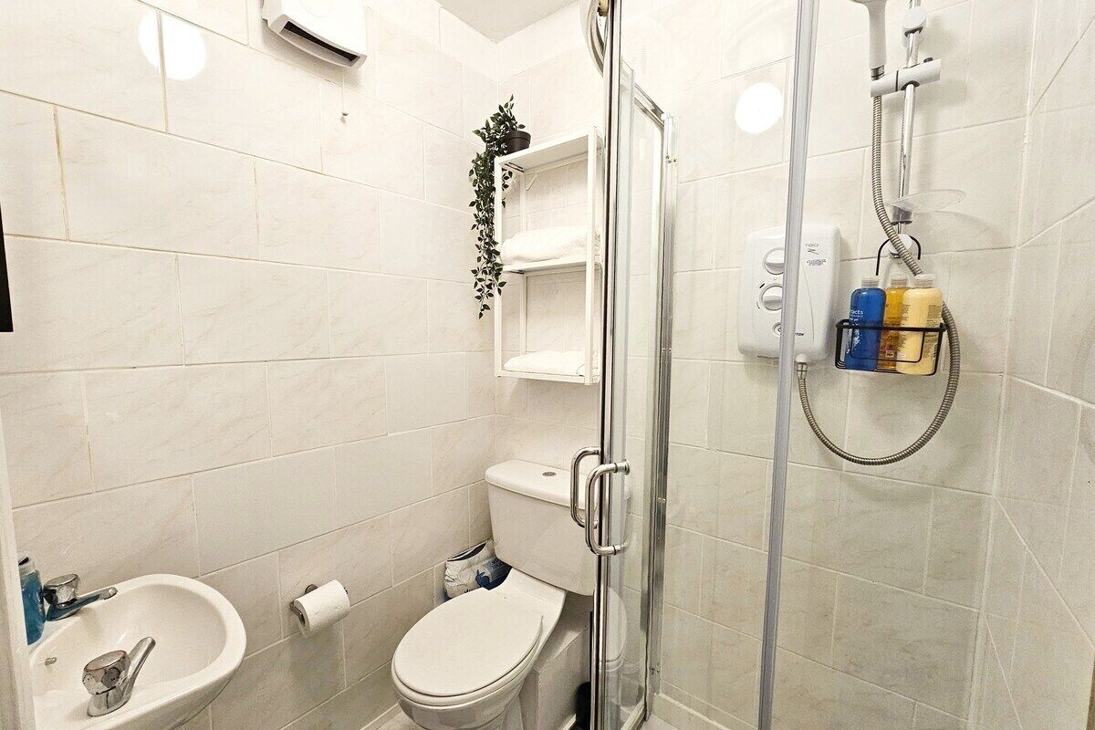 A bathroom with a glass shower enclosure, a toilet, a sink, and a shelf with toiletries.