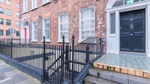 A brick building with a black metal fence, a red door, and a black door with a green exit sign. - Cosy citycentre flat with TV & Wi-Fi included (Dublin 1)
