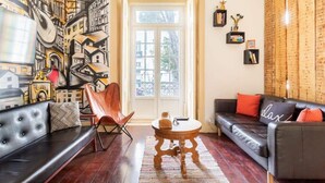 Ein Wohnzimmer mit einer schwarzen Ledersofa, einem Holztisch, einem roten Sessel und einer Wandmalerei mit Stadtansicht.