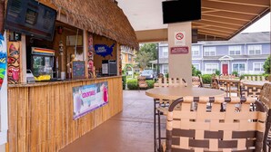 Un bar de style tiki avec un toit de chaume, un tableau affichant le menu et une enseigne publicitaire pour les cocktails.