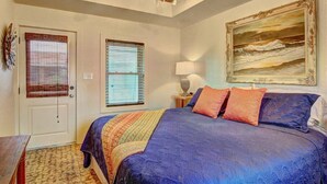 A bedroom with a large bed, two windows, a painting, and a lamp.