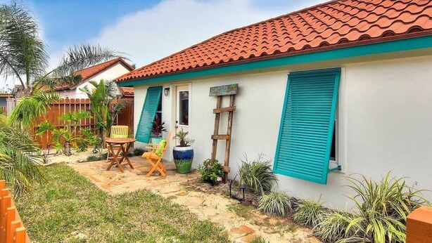 A house with a tiled roof, a small patio with a chair and a table, and a wooden fence.