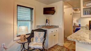 A kitchen with a window, a chair, a table, a TV, and a counter.