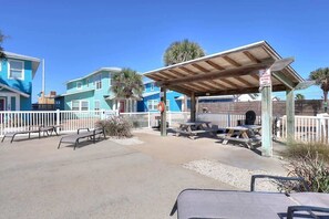 Un patio frente a la playa con mesas de picnic y una zona de estar cubierta.