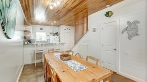 Un coin repas avec une table et des chaises en bois, une cuisine à l’arrière-plan et un escalier menant à un autre niveau.