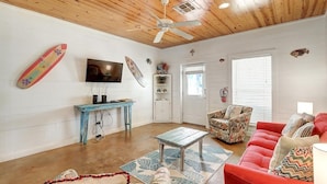 Un salon avec un plafond en bois, un téléviseur, une table bleue, un canapé rouge et un tapis à motifs.