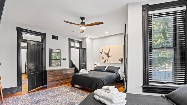 Un dormitorio moderno con una cama grande, un ventilador de techo, vistas del exterior a través de una ventana y una escalera que conduce a otra habitación.