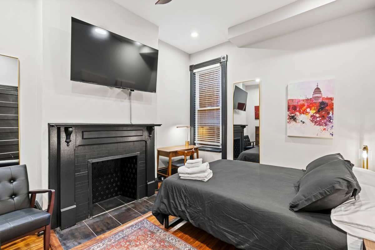 Una habitación de hotel moderna con una cama grande, un televisor de pantalla plana montado en la pared, una chimenea y un cuadro del Capitolio.