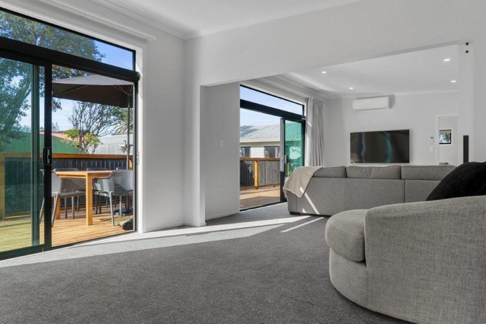 A modern living room with a grey sofa, a TV, and large windows.
