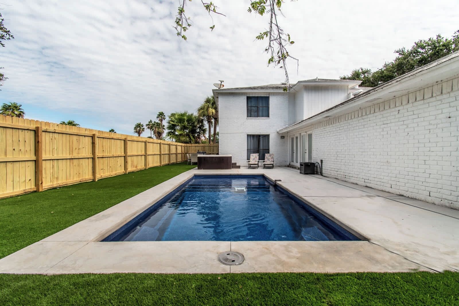 A backyard with a swimming pool, a wooden fence, and a white building.