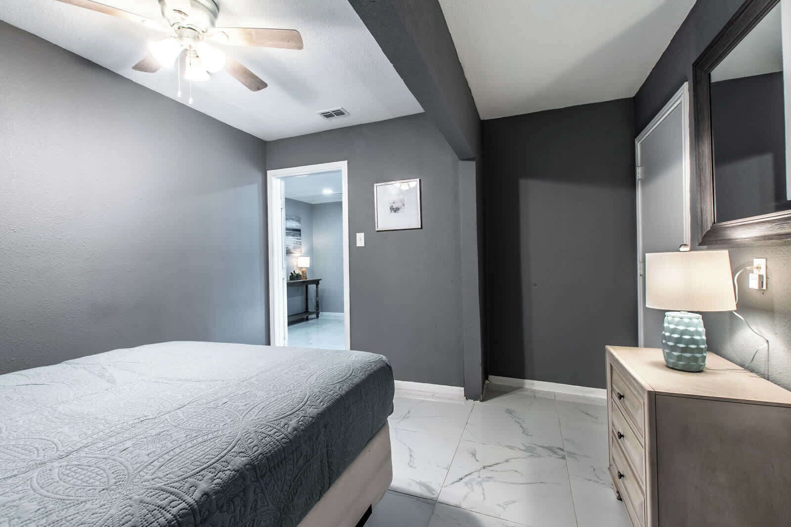 A bedroom with a bed, a dresser, a mirror, and a ceiling fan.