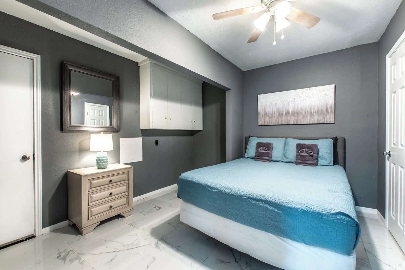 A bedroom with a bed, a nightstand, a ceiling fan, and a wall-mounted cabinet.