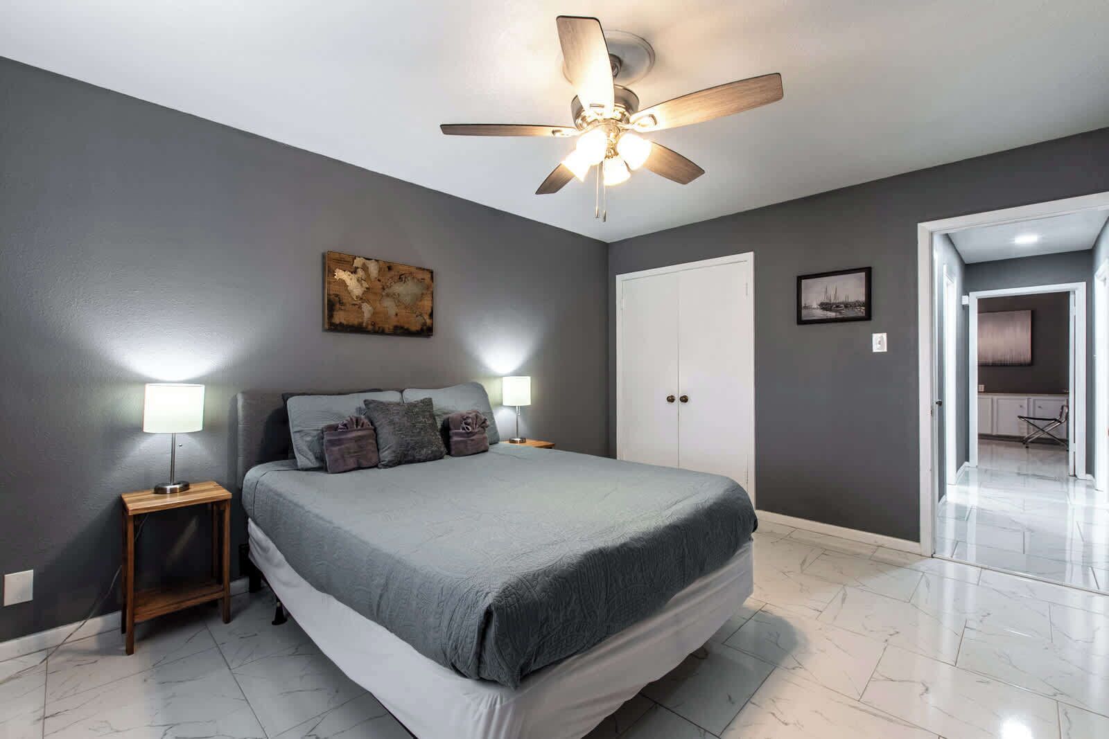 Una camera da letto con un letto, due comodini con lampade, una ventola a soffitto, un armadio e un quadro appeso al muro.