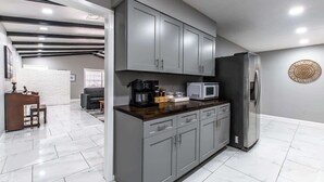 A modern kitchen with grey cabinets, a stainless steel refrigerator, and a coffee maker. - Sleep 29 - Oceanfront Retreat 2 Homes for 29-Guests! (Corpus Christi)