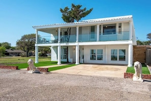 Un edificio blanco de dos pisos con un balcón en el nivel superior, una entrada para vehículos y dos estatuas de leones en la fachada.