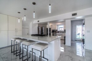 A modern kitchen with a large island, bar stools, pendant lighting, and a view to the outdoor patio.