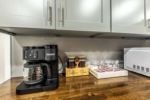 Una barra de café con una cafetera Keurig, tarros de café y una taza sobre una encimera de madera.