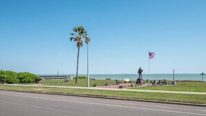 A coastal road with a statue, benches, and an American flag. - Sleep 29 - Oceanfront Retreat 2 Homes for 29-Guests! (Corpus Christi)
