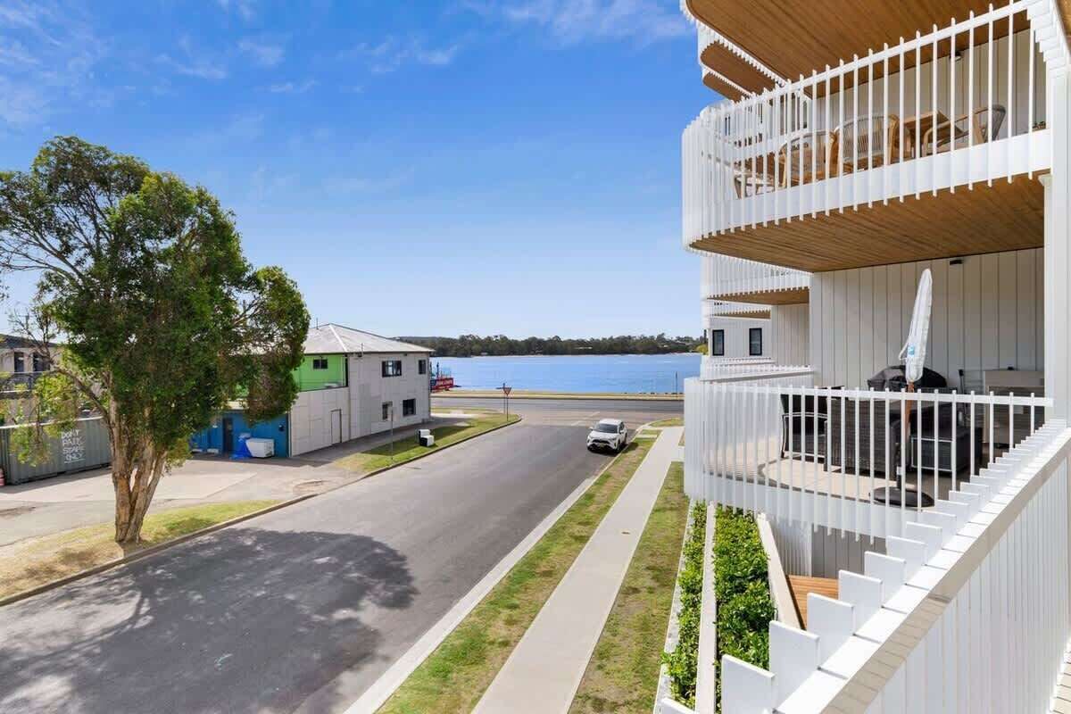 Un bâtiment moderne doté d’un balcon, situé près d’une route et d’un arbre.