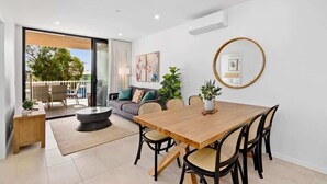 Een moderne woonkamer met een houten eettafel, zwarte stoelen, een ronde spiegel en een bank met kussens.