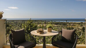 Un balcon avec deux fauteuils en osier, une table ronde et une vue sur la mer.