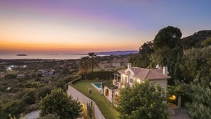 Une propriété située sur la côte, dotée d’une piscine, d’une terrasse et offrant une vue sur la mer au coucher du soleil.