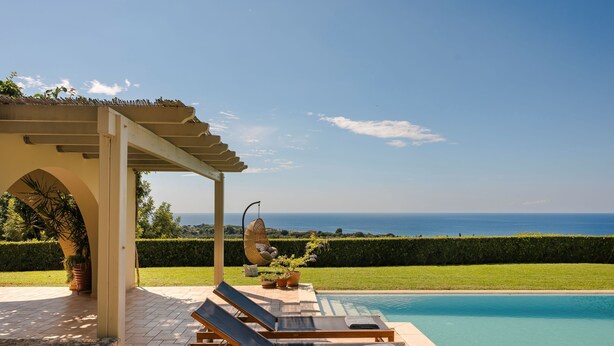 Un espace aménagé au bord de la piscine, comprenant deux chaises longues, une pergola et une vue sur la mer.