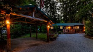 Un rustico chalet con veranda coperta e vialetto sterrato che conduce a un pontile di legno.
