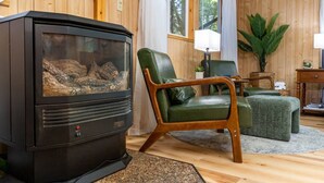 Un accogliente soggiorno con rivestimento in legno, un camino a legna nero, poltrone in pelle verde e una pianta grande.